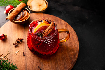 A glass mug of mulled wine on the black background and Christmas decorations. Festive winter drink
