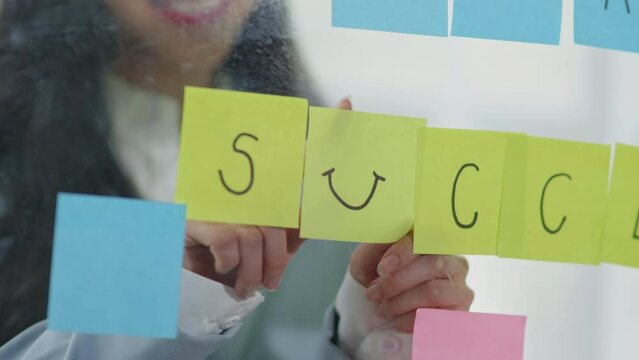 Businesswoman in suit write success on Post-it sticky notes and paste on the board for business planning and marketing.