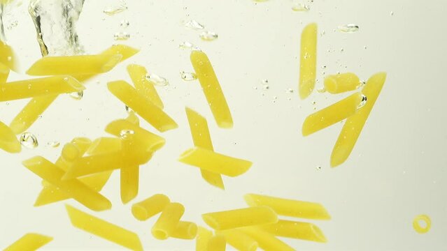 Slow Motion of Penne rigate pasta splash falling into boiled water on white background