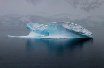 Iceberg in dead calm water near the Antarctic Peninsula. Blue ice; reflection on water. 
