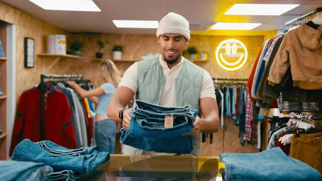 Smiling male sales assistant sorting stock of denim jeans in pop up fashion or clothes store - shot in slow motion