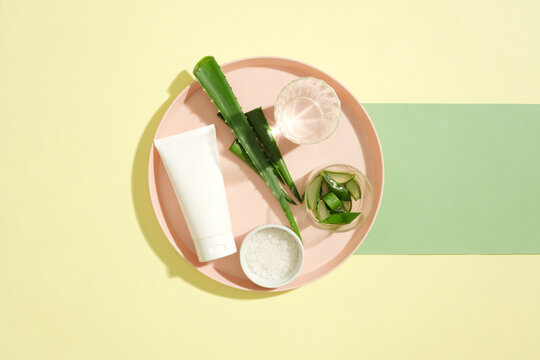 A tube of unbranded facial cleanser and props are displayed on a pink ceramic plate. Aloe vera contains high levels of cinnamic acid, which has antiseptic effects on the skin and prevents inflammation