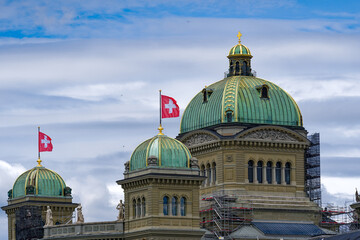 Tower with green copper dome of Swiss Federal Palace with waving Swiss flag on top on a cloudy summer day at Bern, Capital of Switzerland. Photo taken July 1st, 2023, Bern, Switzerland.