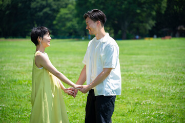 Fototapeta na wymiar Beautiful Asian couple laughing and frolicking happily hand in hand in a lush green park. 
