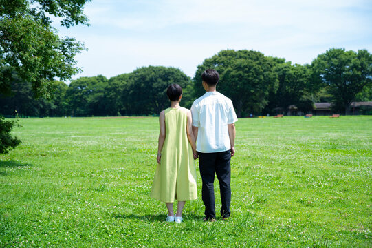 Backshot of a couple holding hands and smiling happily in a beautiful green park. 