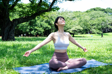 Beautiful Asian woman smiling and doing yoga in a beautiful grassy park. Urban living, wellbeing, mental health, happiness, environmental concern.