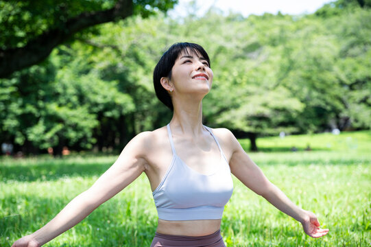 Beautiful Asian woman smiling and doing yoga in a beautiful grassy park. Urban living, wellbeing, mental health, happiness, environmental concern.