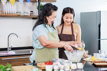 Asian female baker pastry bakery chef daughter wears apron standing smiling helping old senior...