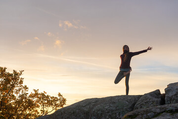Woman doing yoga pose on a mountain at sunset