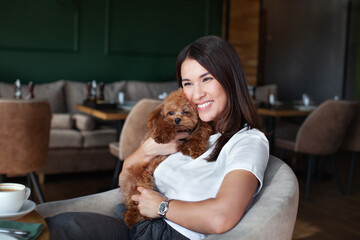 Portrait of smiling woman hugging dog while sitting at table in restaurant or cafe. Relationships...