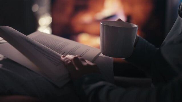 Close-up of a Cup of Tea and a Book in the Hands of a Person by the Fireplace