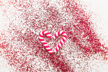 Christmas composition with candy canes in form oh heart on blue wooden background with red sequins