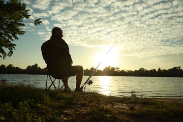 Fisherman with rod sitting on folding chair and fishing at riverside, space for text