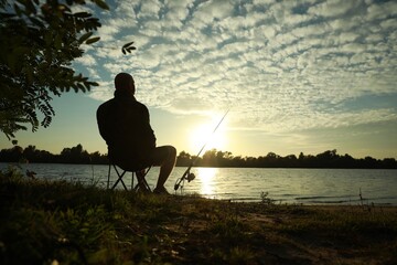 Fisherman with rod sitting on folding chair and fishing at riverside, space for text