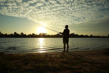 Fisherman with rod fishing at riverside at sunset