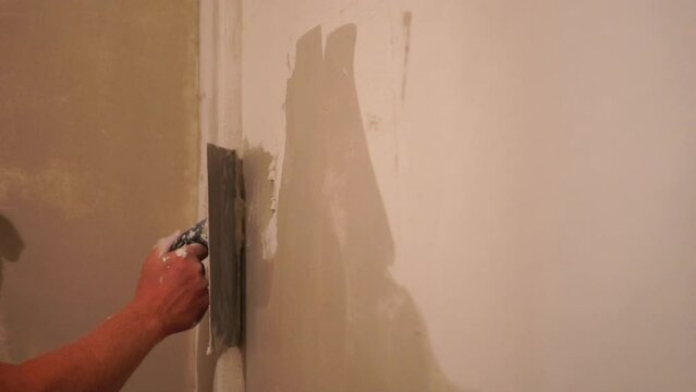 Male builder use metal spatula for putty walls, repairman filling spatula with spackling paste and covering cement wall surface. Builder leveling wall and angle Renovation work in Residential Premises