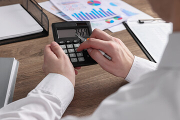 Man using calculator at wooden table, closeup