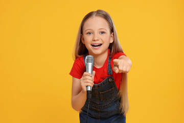Cute little girl with microphone singing on yellow background