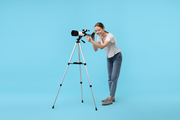 Young astronomer looking at stars through telescope on light blue background