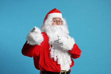 Merry Christmas. Santa Claus pointing at something on light blue background