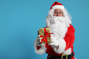 Santa Claus holding Christmas gift on light blue background, space for text