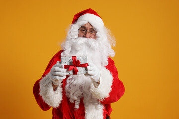 Fototapeta na wymiar Santa Claus holding Christmas gift on orange background