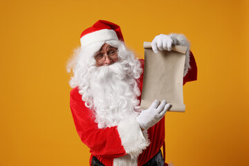 Naklejka premium Merry Christmas. Santa Claus showing blank paper sheet on orange background