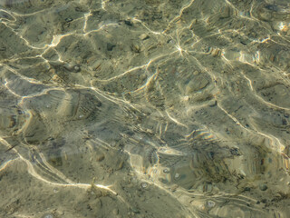 Crystal clear transparent water with fine white sand base with bright reflection of sun in water movement. Lines and shapes in nature