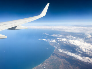 Aerial view of ocean through a plane window. Wing of airplane with blue sky and beauty clouds over...