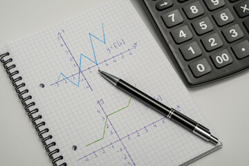 Wykresy narysowane w zeszycie od matematyki, obok leży kalkulator