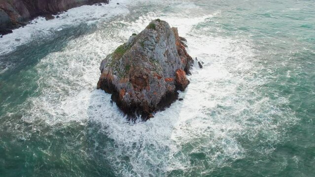 Scoglio il Morto, Sardinia: aerial view in orbit over the famous islet and the waves hitting the rock.