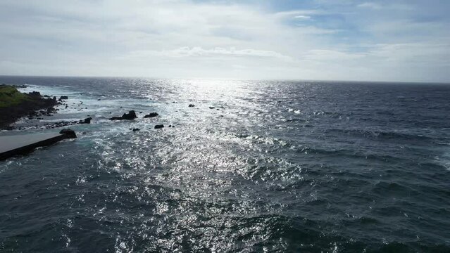 Backward aerial over rugged coast of Zona Balnear do Negrito, Azores. Seagul flying at sunset