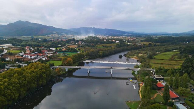 Stunning aerial 4K drone footage of a village - Ponte de Lima in Portugal and its iconic landmark - Stone roman bridge crossing over the Lima River. Filmed in autumn during partly cloudy weather.
