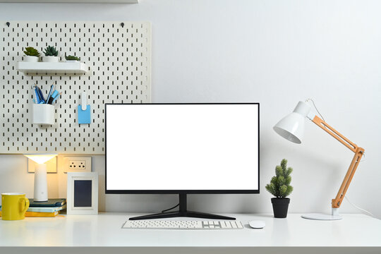 Home office desk with blank computer monitor, picture frame, lamp and peg board on wall
