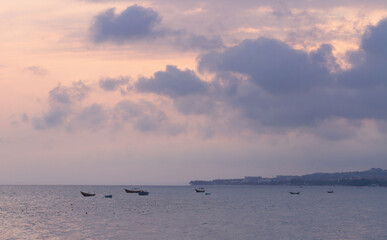 Sunset over the sea in Vietnam. Seascape in beautiful pink and purple tones. Small fishing boats against the background of the coastline