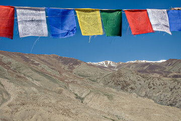 Close uo photograph of prayer flags with snow claded mountain and blue sky in background in Leh, India.