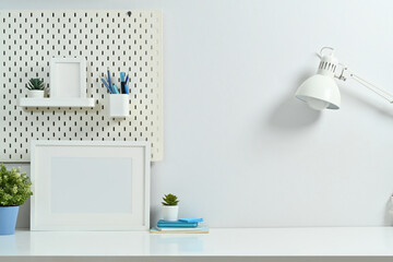 Stylish working desk with picture frames, books, lamp, potted plants and peg board on wall