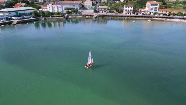 High drone footage of a sailboat sailing neat to fishing port of Aldan in Pontevedra, Galicia, Spain