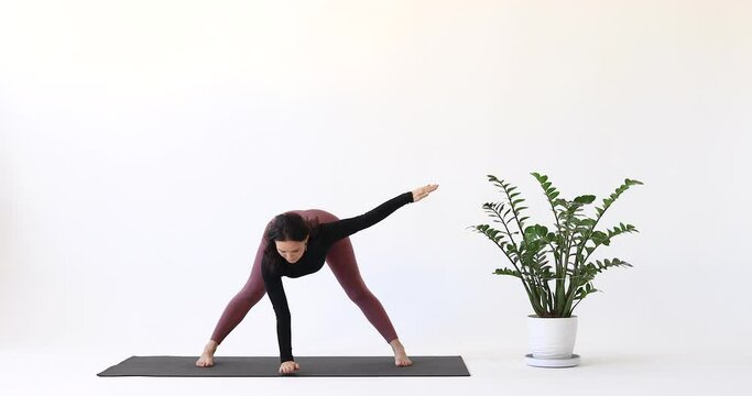 Yoga instructor performing Parivritta Ardha Prasarita Padottanasana exercise, intense stretching pose, training in leggings and long sleeve short top while standing on mat in studio