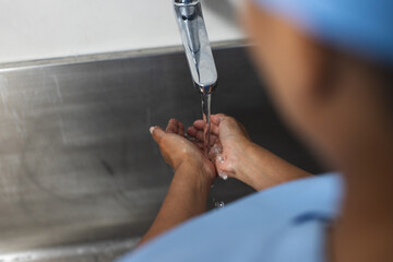 Midsection of biracial female doctor wearing scrubs washing hands in operating theatre