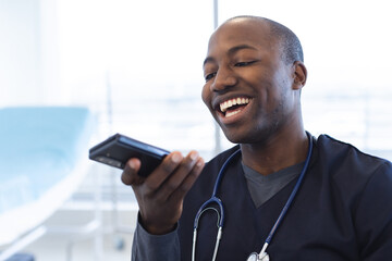 Happy african american male doctor talking on smartphone at desk in hospital