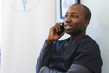 African american male doctor talking on smartphone in waiting room in hospital, copy space