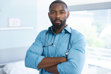 Portrait of happy african american male doctor wearing blue shirt and stethoscope in hospital room