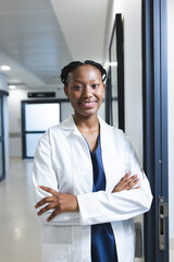 Portrait of happy african american female doctor wearing lab coat in hospital corridor