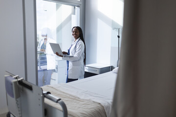 Portrait of happy african american female doctor using laptop in hospital room, copy space