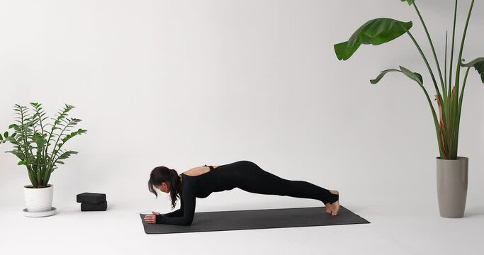 Woman yoga instructor performs various variations of Vasishthasana exercise, side plank pose, training in a sporty black long-sleeved jumpsuit on a mat in the studio