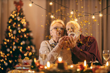 A festive senior couple is sitting at home on christmas and new year's eve at dining table and...