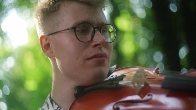 Close-up caucasian man stroking the violin string with bow, playing outdoors
