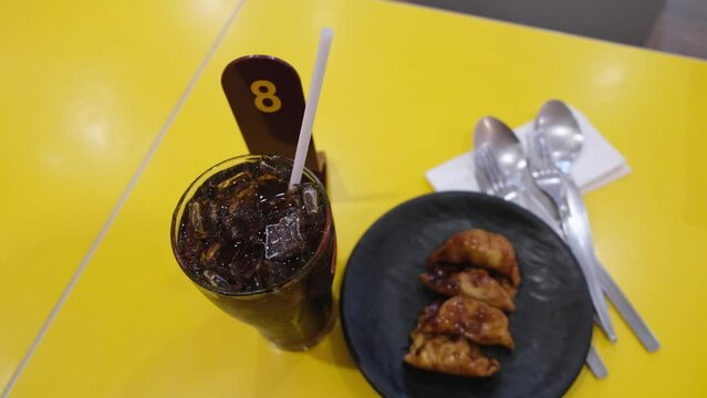 Cola drink in a glass with ice and some dumplings on a small dish with a queue number eight, two pair of spoon and fork. Food and Beverage.