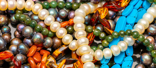 Beads and necklaces made of colored semi precious stones. Background from a variety of beautiful jewelry, multi-colored turquoise stones, amber, cat's eye, pearls. - obrazy, fototapety, plakaty